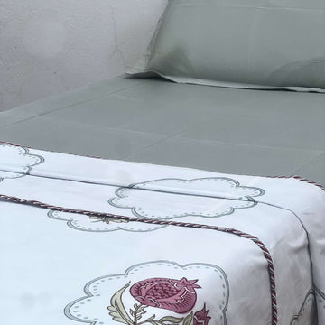 Bed with white bedding featuring floral embroidery and a gray pillow against a plain wall.