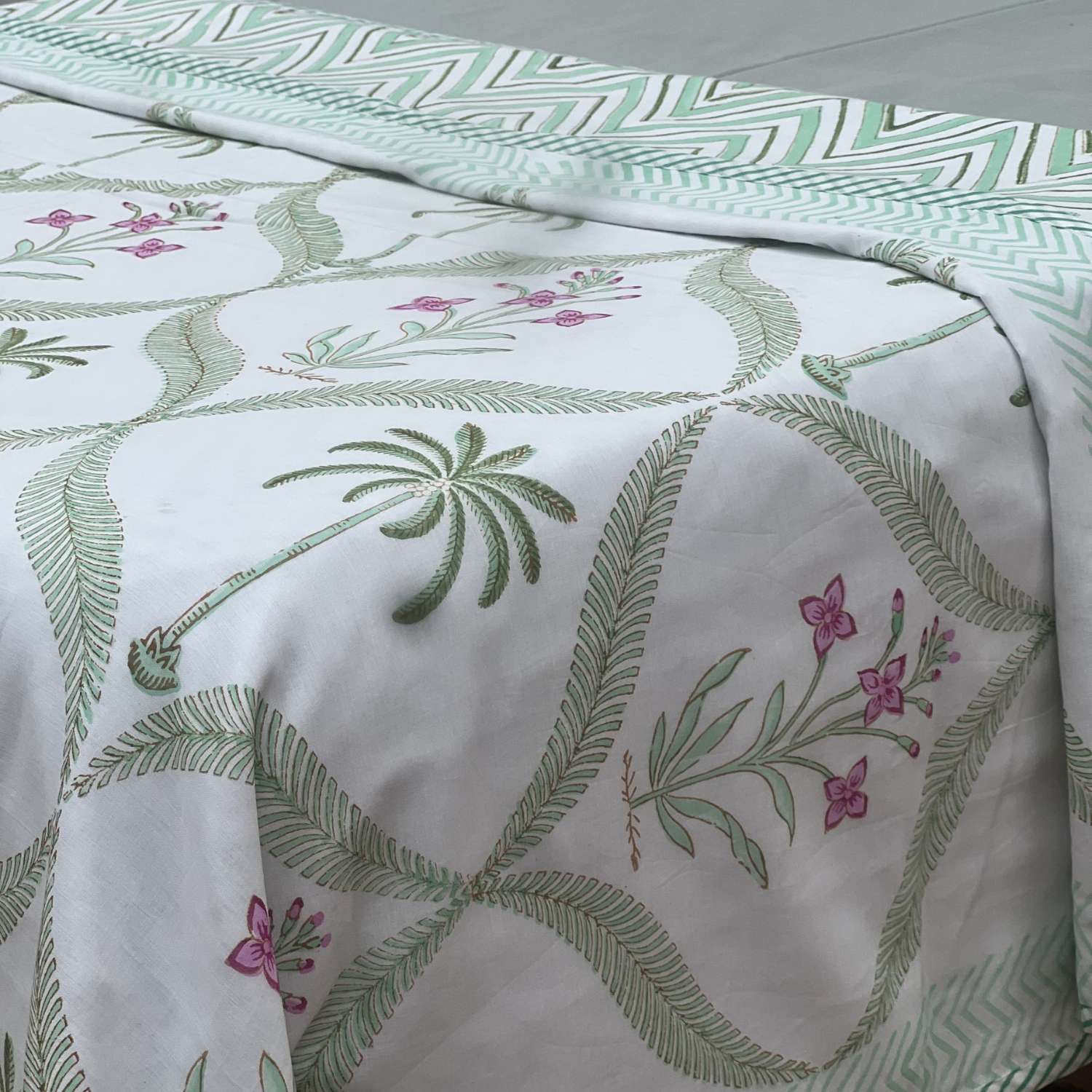 Bed with green and white patterned bedding featuring palm trees and flowers.