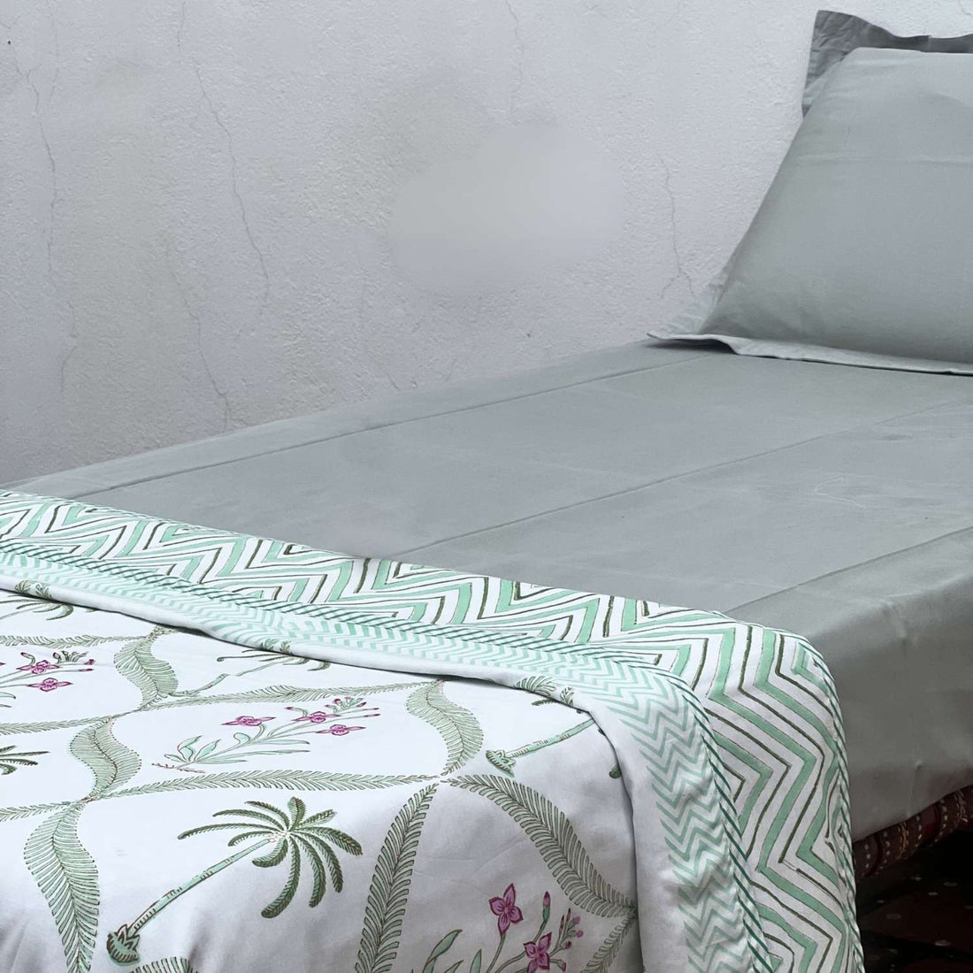 Bed with green and white patterned bedding featuring palm trees and flowers.