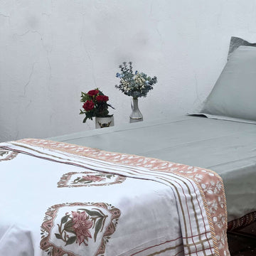 Bed with floral-patterned bedspread in a room with a white wall and small decorative plants.